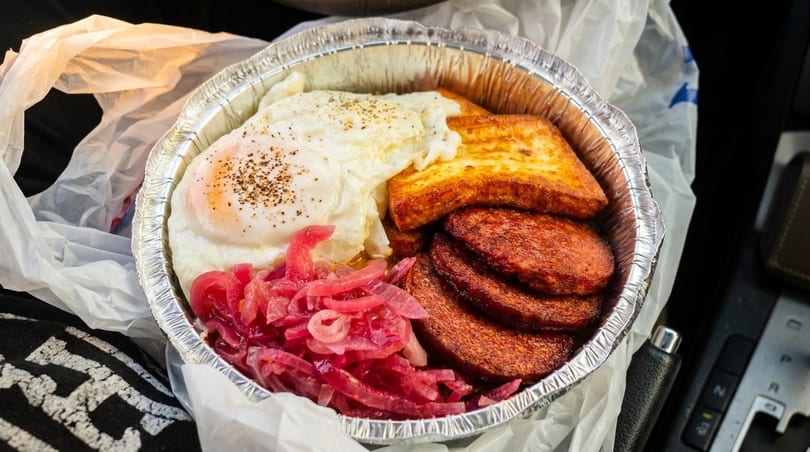 A takeout container with fried eggs, halloumi cheese, chorizo, and pickled red onions.