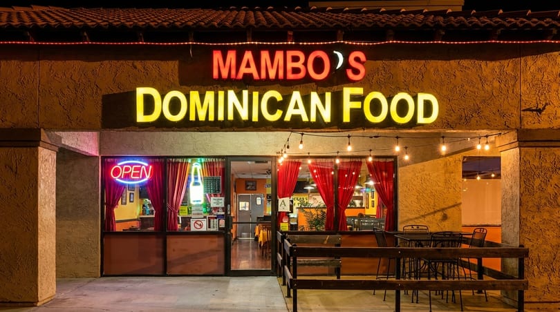 Mambo's Dominican Food restaurant exterior at night with glowing signs and outdoor seating.