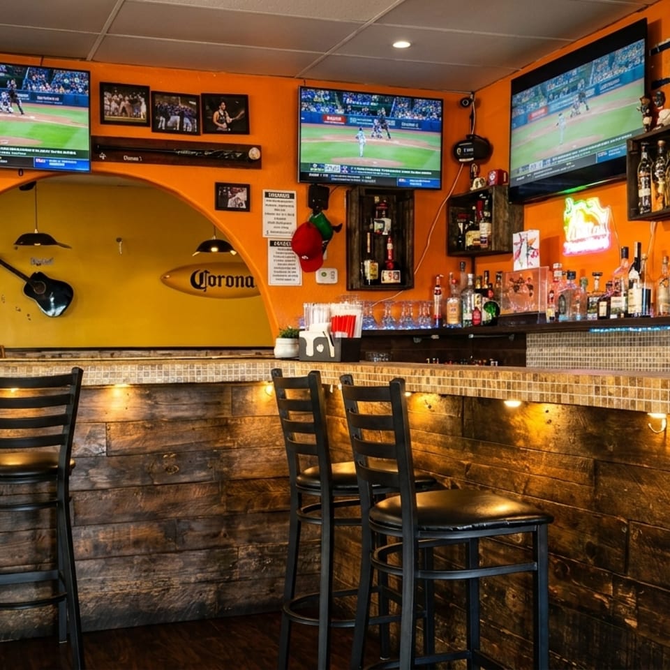 A vibrant bar with orange walls, multiple TVs, a tiled counter, and liquor bottles.